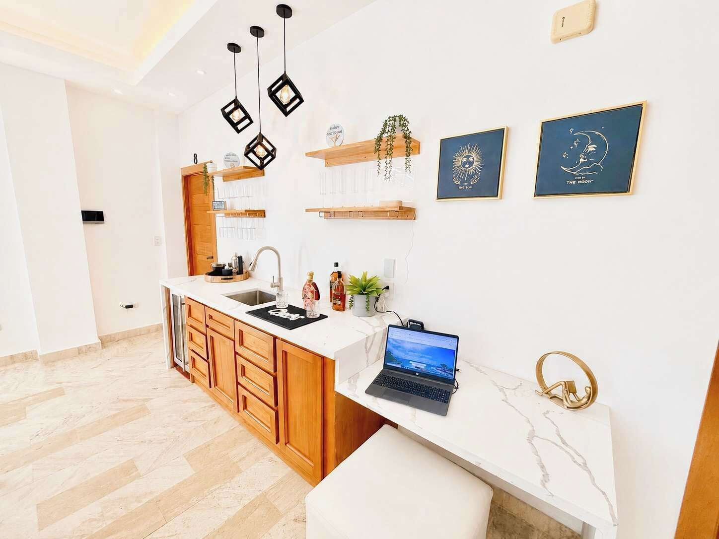 A modern kitchen with a marble countertop, wooden cabinets, a laptop, and decorative wall art.