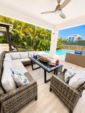 A covered outdoor seating area with wicker furniture and a pool in the background. - Sunset Villa | Bunk Room, Pool & Sleeps up to 11 (Sosúa)