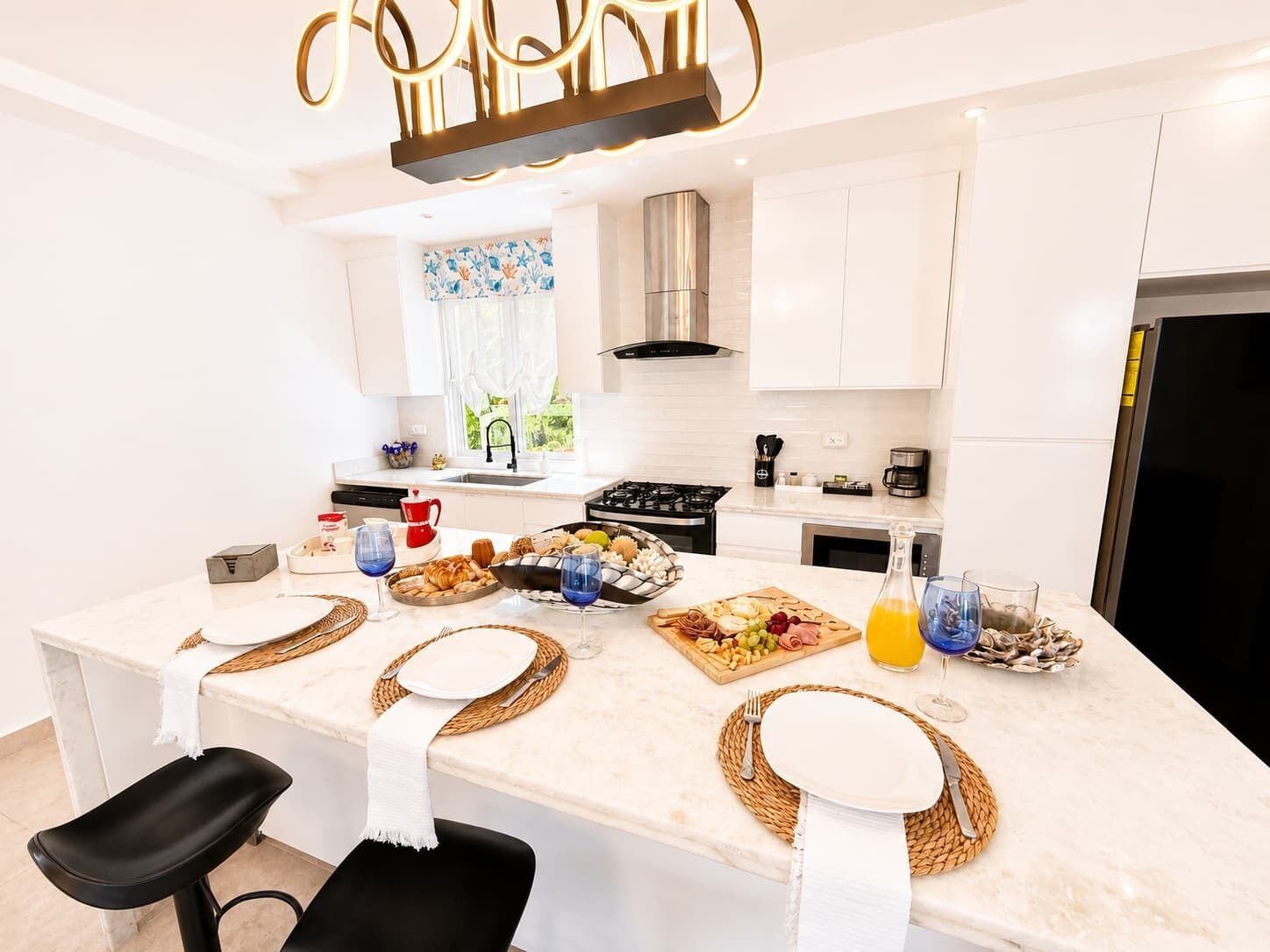 Une cuisine moderne dotée d’un îlot central, de meubles blancs, d’appareils électroménagers en acier inoxydable et offrant une vue sur l’extérieur.
