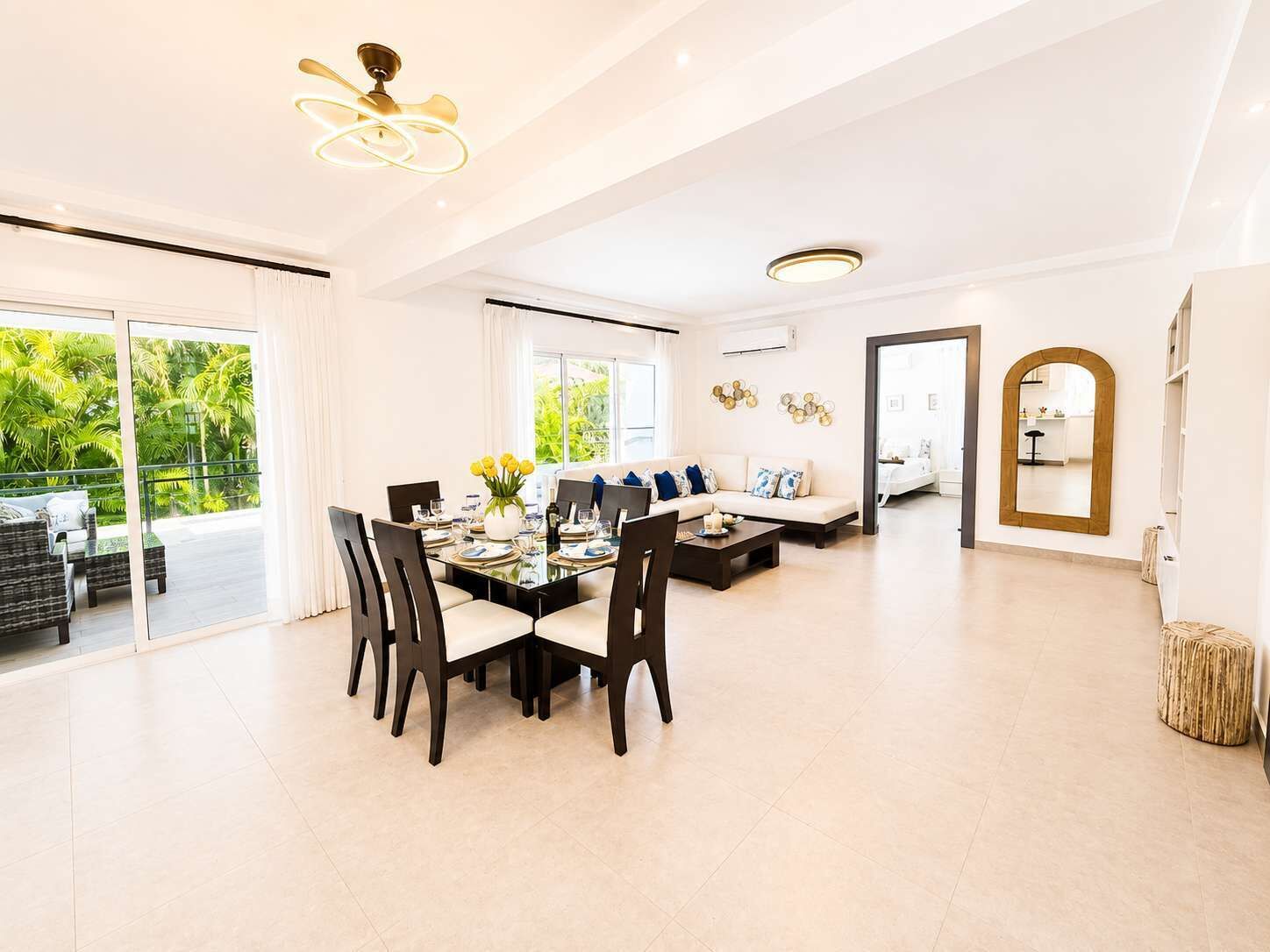 A spacious living area with a dining table set for four, a sofa, and a large window offering a view of greenery.