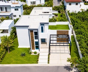 A modern two-story house with a flat roof, a front entrance with a glass door, and a small front yard with a palm tree. - Sunset Villa | Bunk Room, Pool & Sleeps up to 11 (Sosúa)