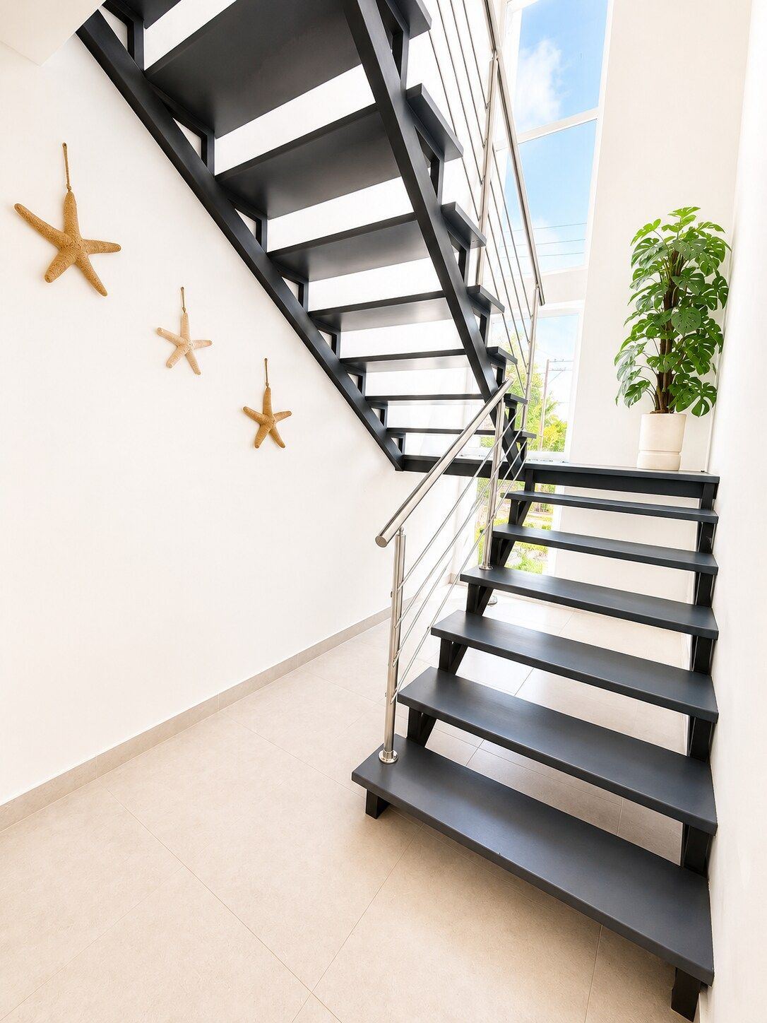 Eine moderne Treppe mit schwarzen Stufen und einem Metallgeländer, die zu einem Balkon mit Blick auf den Himmel führt.
