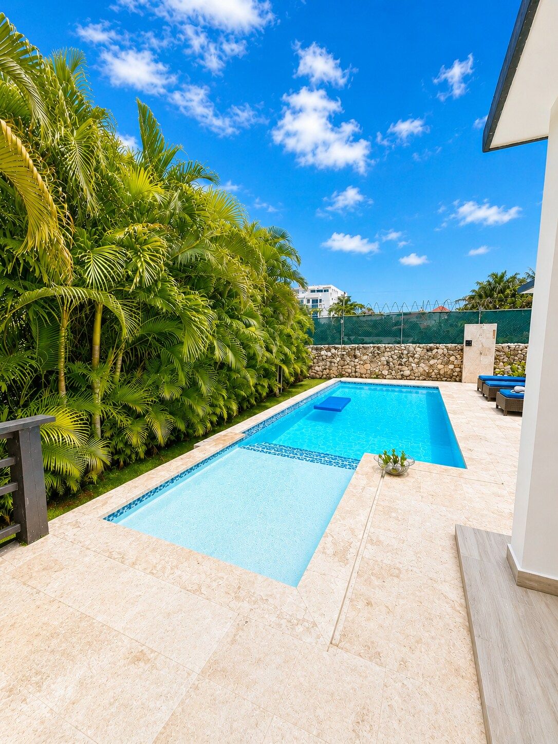 Une piscine dotée d’une terrasse carrelée, entourée d’une végétation luxuriante et d’un mur en pierre.
