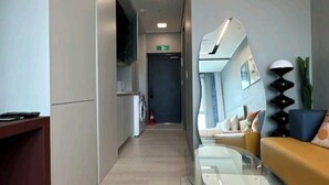 Moderni hotellin aula, jossa on keittiöalue, sohva ja lasipöytä.