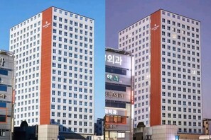 A multi-story hotel building with a uniform facade, numerous windows, and a prominent red vertical stripe. - The Bayment Rasidence (Busan)