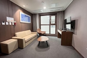 A hotel room with a sofa, armchair, coffee table, TV, and a large window. - The Bayment Rasidence (Busan)
