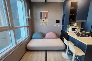 A compact room with a built-in bench, a kitchenette, and a large window. - The Bayment Rasidence (Busan)