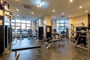 A gym with various exercise equipment, large windows, and a tiled floor. - The Bayment Rasidence (Busan)
