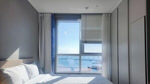Hotellihuone, jossa on suuri ikkuna, sänky ja yöpöytä.