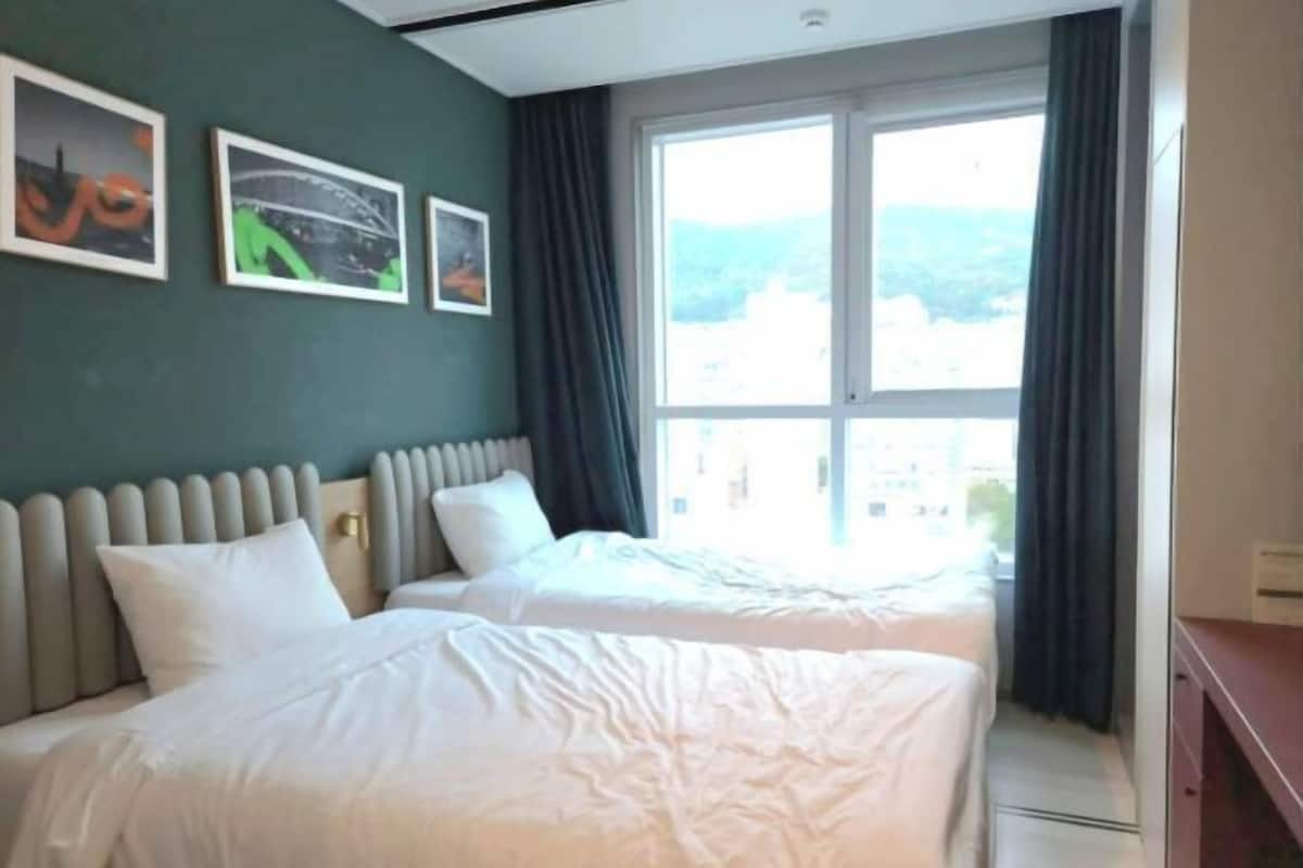 A hotel room with two beds, a large window with curtains, and three framed pictures on the wall.