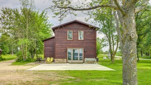 A rustic wooden cabin with a large sliding glass door, surrounded by a grassy area and trees.