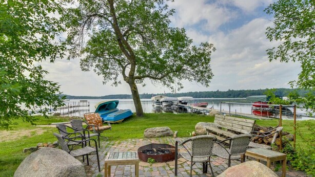 An outdoor seating area with stone flooring, a fire pit, and a view of a lake with boats.