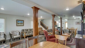 A spacious living room with a wooden dining table, several chairs, and a staircase leading to another level.
