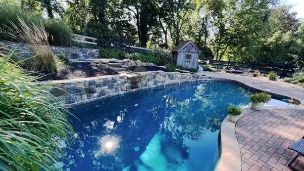 Una piscina con bordo in pietra, circondata dal verde e da una piccola struttura in legno.