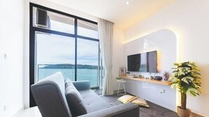 Una sala moderna con un sofá, un televisor de pantalla plana, una mesita, una planta en maceta y vista al mar.