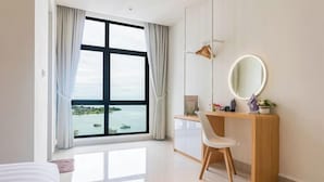 Una habitación de hotel con un ventanal grande, un escritorio de madera, una silla, un espejo redondo y una cama.