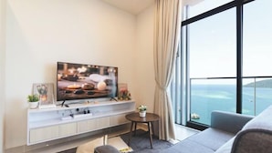 Una sala de estar moderna con un televisor de pantalla plana, un sofá, una mesita y vistas al mar a través de amplios ventanales.