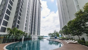 Un edificio moderno con zona de piscina, que incluye una terraza de madera y sillones de descanso.