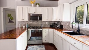 Une cuisine moderne avec des meubles blancs, un four en acier inoxydable, un four à micro-ondes et une cuisinière à gaz. Une fenêtre offre une vue sur la verdure environnante.
