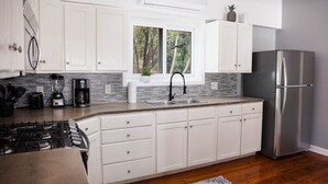 Una cocina moderna con armarios blancos, un refrigerador de acero inoxidable y una ventana con vistas a árboles.