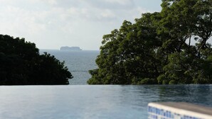 Vue depuis un espace aménagé au bord de la piscine, offrant une vue dégagée sur l’océan et un navire au loin.