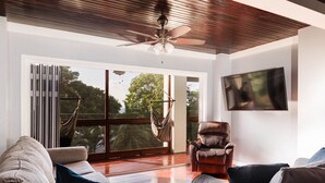 Un vaste salon doté d’une grande porte-fenêtre coulissante donnant sur un balcon, d’un ventilateur de plafond et d’un téléviseur à écran plat fixé au mur.