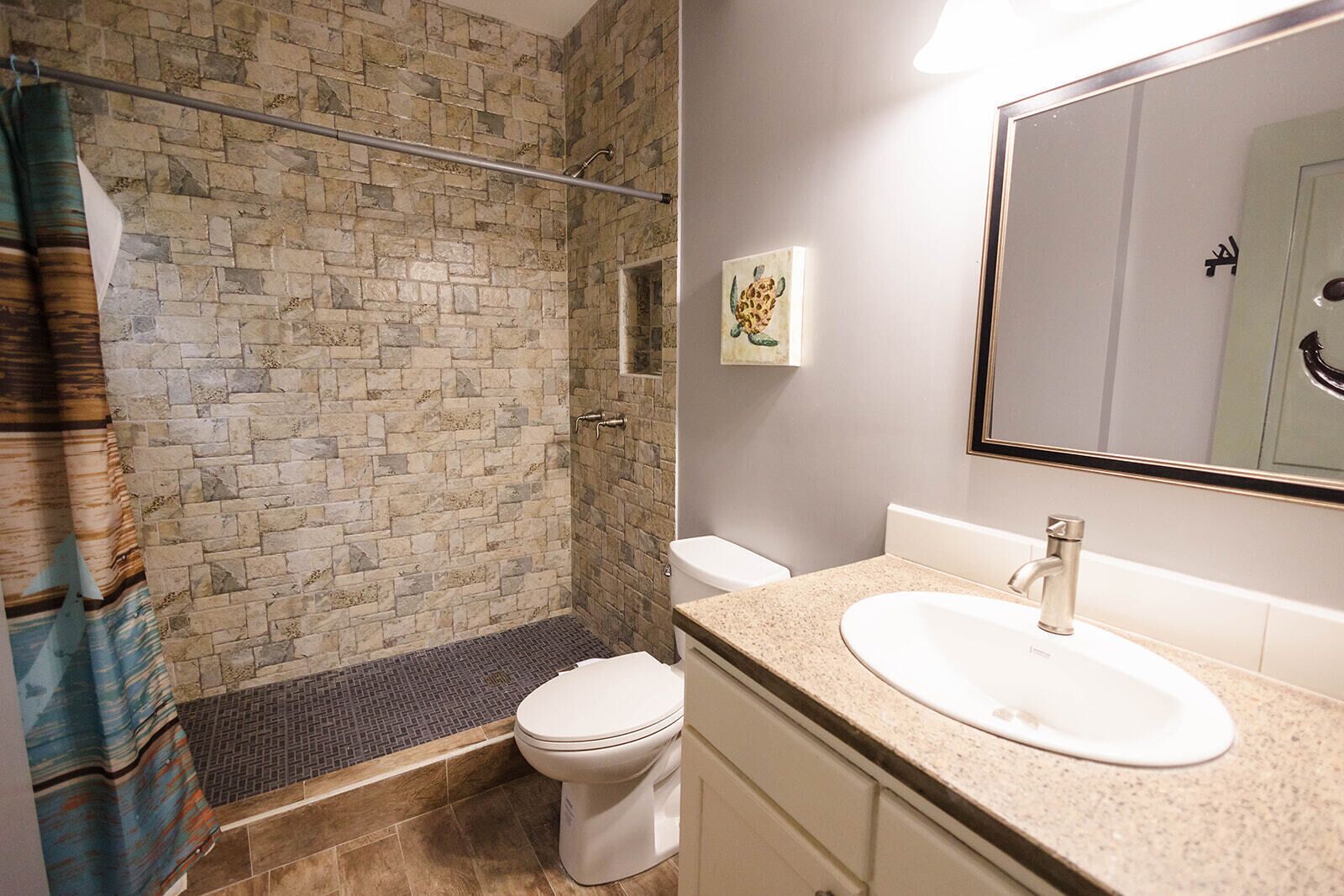 Une salle de bain avec un mur en pierre, une douche, des toilettes et un lavabo avec un miroir.