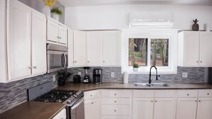 Una cocina moderna con armarios blancos, estufa a gas, horno integrado, cafetera y ventana con vistas a árboles.