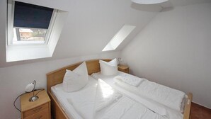 Ein Schlafzimmer mit einem Einzelbett, einem Nachttisch, einer Lampe und einem Fenster mit Blick ins Freie.