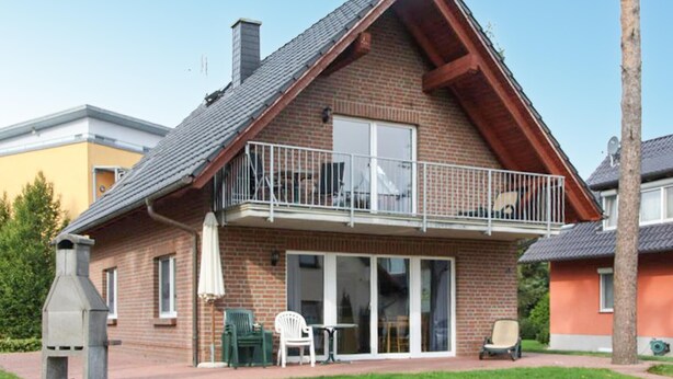 Ein zweistöckiges Haus mit einem Balkon, einer Terrasse und Gartenmöbeln sowie einem Schornstein.