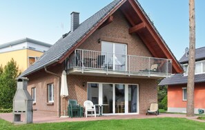 Ein zweistöckiges Haus mit einem Balkon, einer Terrasse und Gartenmöbeln sowie einem Schornstein.