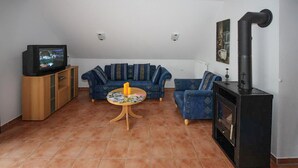 Ein Wohnzimmer mit einer Sofagarnitur, einem Fernseher, einem Tisch mit Zeitschriften und einem Kaminofen.