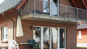 Ein zweistöckiges Gebäude mit Balkon, einer Schiebetür aus Glas und einer Terrasse mit Tisch und Stühlen.