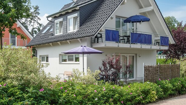 Ein zweistöckiges Haus mit einem geneigten Dach, einem Balkon mit blauen Vorhängen und einem violetten Regenschirm.