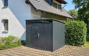 A dark-colored metal shed with a door, located in front of a house with a tiled roof and a window. - 3 bedroom stunning apartment in Röbel (Röbel)