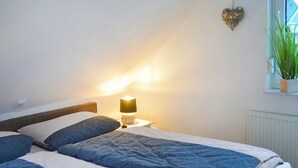 A bedroom with a bed, pillows, a bedside table with a lamp, a window with a plant, and a radiator. - Awesome apartment in Röbel with lake view (Röbel)