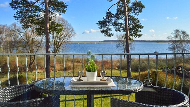 A glass table with chairs and a potted plant on a balcony overlooking a body of water. - Awesome apartment in Röbel with lake view (Röbel)