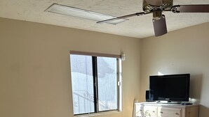 A bedroom with a bed, a dresser, a television, a ceiling fan, and a window. - Cozy 1-bedroom house in peaceful Sun City West with AC (Sun City West)