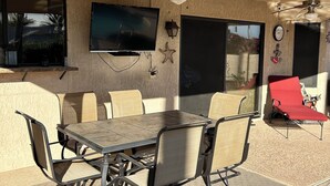 An outdoor patio with a table and chairs, ceiling fans, a TV mounted on the wall, and a red chair. - Cozy 1-bedroom house in peaceful Sun City West with AC (Sun City West)