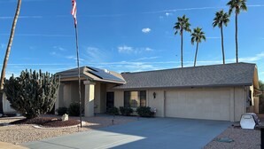 A single-story house with a garage, a large cactus in the front yard, and a flagpole with an American flag. - Cozy 1-bedroom house in peaceful Sun City West with AC (Sun City West)