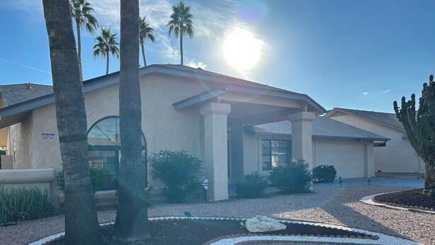 A building with a covered entrance, palm trees, and a clear sky. - Cozy 1-bedroom house in peaceful Sun City West with AC (Sun City West)