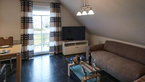 Un salon comprenant un canapé, une table basse, un téléviseur posé sur un meuble et un coin repas avec une table et des chaises.