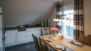 Un coin repas avec une table en bois dressée pour quatre personnes, un vase rempli de fleurs et un comptoir de cuisine équipé d’appareils électroménagers.