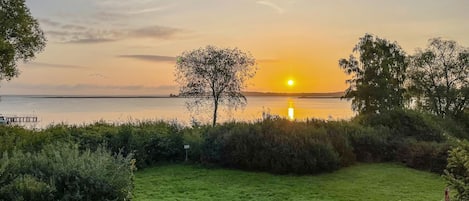 Un champ verdoyant avec une étendue d’eau et un coucher de soleil en arrière-plan.
