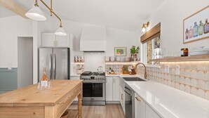 Eine moderne Küche mit weißen Schränken, Edelstahlgeräten, einem Holztisch und Pendelleuchten.