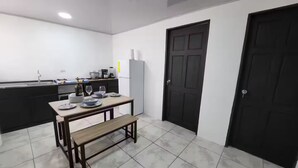 A compact kitchen with a dining table set for two, a bench, and a refrigerator. - A 5 minutos Parque Nacional Manuel Antonio A/C #2 (Quepos)