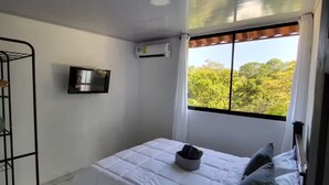 A single bed with a white duvet, a grey hat on the bed, and a TV mounted on the wall. - A 5 minutos Parque Nacional Manuel Antonio A/C #2 (Quepos)