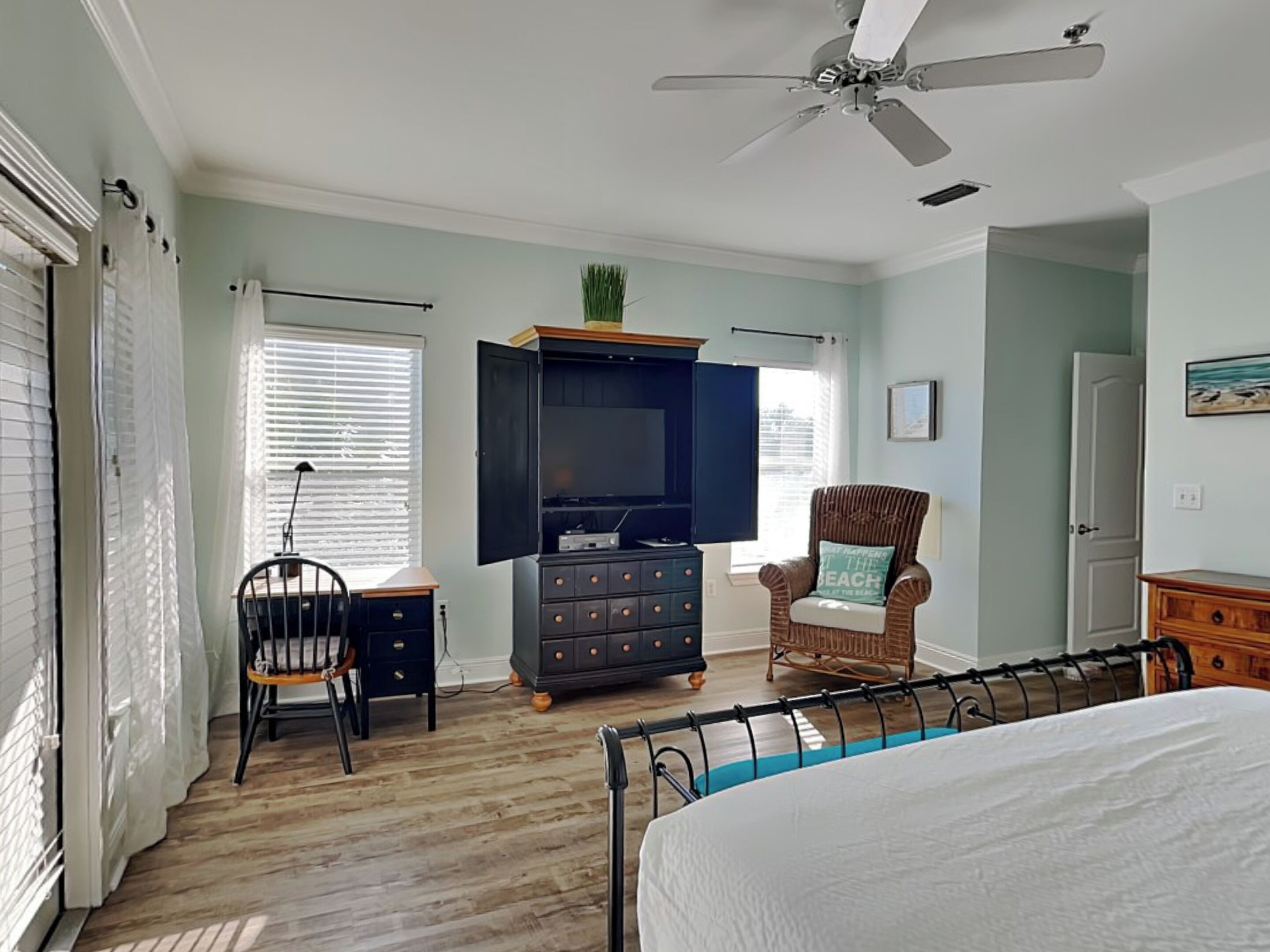 Une chambre à coucher comprenant un lit, un téléviseur, une commode, une chaise et un ventilateur de plafond.
