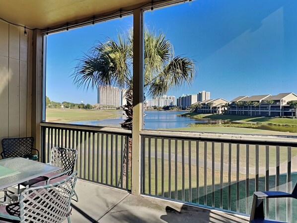 A balcony with a view of a lake, palm trees, and buildings in the distance. - Seascape Condo #407 (Miramar Beach)