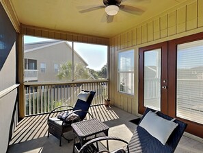 A covered porch with a ceiling fan, two chairs, a small table, and a sliding glass door. - Seascape Condo #407 (Miramar Beach)